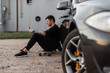 © alones - handsome hipster man in black clothes with a smartphone sits and rest on a longboard near the car