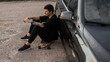 © alones - Hipster handsome man model with black clothes and sneakers sits and rest on longboard near a black car. Summer weekend