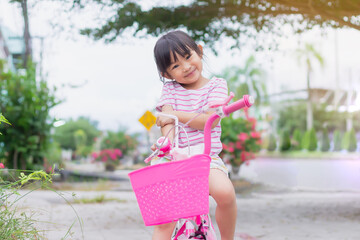 Wall Mural - Portrait image of 4-5 years old kid. Happy Asian child girl ride a bike at the park outdoor. Exercise for health and sport. Summer season.