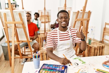 Sticker - Young african man at art studio smiling happy and positive, thumb up doing excellent and approval sign