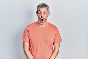 Handsome middle age man with grey hair wearing casual t shirt afraid and shocked with surprise expression, fear and excited face.