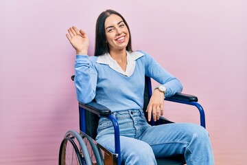 Poster - Beautiful woman with blue eyes sitting on wheelchair waiving saying hello happy and smiling, friendly welcome gesture