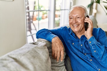 Canvas Print - Senior man with grey hair sitting on the sofa at the living room of his house having a conversation speaking on the phone