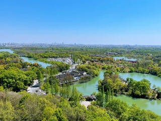 Aerial view of a small lake surrounded by green trees and black roof houses under a blue sky