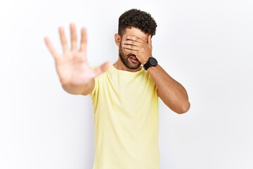 Wall Mural - Arab young man standing over isolated background covering eyes with hands and doing stop gesture with sad and fear expression. embarrassed and negative concept.