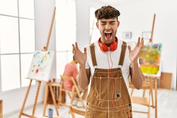 Canvas Print - Young hispanic man at art studio celebrating mad and crazy for success with arms raised and closed eyes screaming excited. winner concept