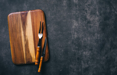 Wall Mural - Cutting board with fork and knife carving on dark stone background. Steak cooking concept