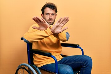 Poster - Handsome man with beard sitting on wheelchair rejection expression crossing arms doing negative sign, angry face