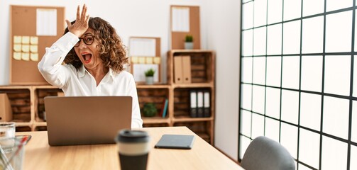 Poster - Middle age hispanic woman working at the office wearing glasses surprised with hand on head for mistake, remember error. forgot, bad memory concept.