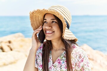 Sticker - Young latin girl wearing summer hat talking on the smartphone at the beach.