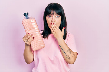 Canvas Print - Young hispanic woman holding detergent bottle covering mouth with hand, shocked and afraid for mistake. surprised expression