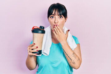 Canvas Print - Young hispanic woman wearing sport clothes drinking a protein shake covering mouth with hand, shocked and afraid for mistake. surprised expression