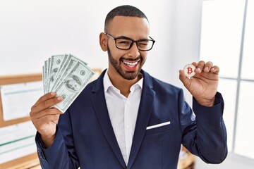 Poster - African american young man holding bitcoin virtual money and dollars banknotes winking looking at the camera with sexy expression, cheerful and happy face.