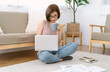 Beautiful Asian woman freelancer wear glasses sitting on the floor with laptop computer working while having mug of morning coffee at home. Cozy home workplace, remote work, New normal concept.
