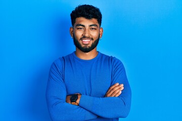 Wall Mural - Arab man with beard wearing casual blue sweater happy face smiling with crossed arms looking at the camera. positive person.