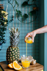 Wall Mural - Caucasian hand pouring juice into the glass with pineapple and orange slices on table