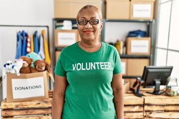 Sticker - Mature hispanic woman wearing volunteer t shirt at donations stand looking positive and happy standing and smiling with a confident smile showing teeth