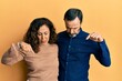 Middle age hispanic couple wearing casual clothes pointing down looking sad and upset, indicating direction with fingers, unhappy and depressed.