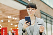 © Seventyfour - Portrait of young woman entering credit card information online into smartphone while standing in shopping mall interior, copy space