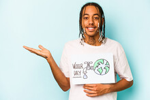 Young African American Man Holding Protect Our Planet Placard Isolated On Blue Background Showing A Copy Space On A Palm And Holding Another Hand On Waist.