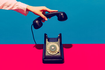 retro objects, gadgets. female hand holding handset of vintage phone isolated on blue and pink backg