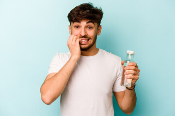 Wall Mural - Young hispanic man holding a bottle of water isolated on white background biting fingernails, nervous and very anxious.