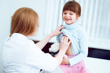 Caucasian female doctor examining patient little girl by stethoscope in office