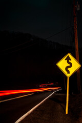 Canvas Print - Vertical long exposure of an empty street at night with car trails and a road sign - dark wallpaper