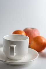 Poster - Closeup shot of a white cup and saucer with oranges and an apple in the background