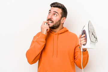 Wall Mural - Young caucasian man holding an iron isolated on white background relaxed thinking about something looking at a copy space.