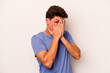 © Asier - Young caucasian man isolated on white background blink through fingers frightened and nervous.