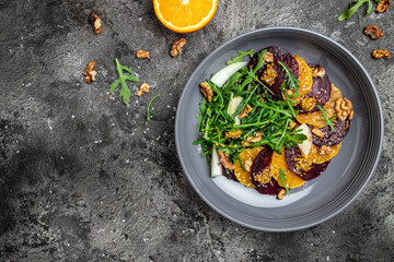 beet salad with arugula, oranges and walnuts on a dark background. Clean eating, dieting, vegan food concept. banner, menu, recipe place for text, top view