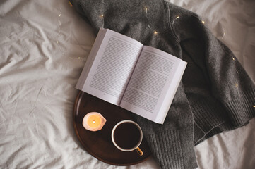 Wall Mural - Cup of coffee with leopard print staying on wooden tray with scented burning candle and open paper book on knitted textile in bed at home. Good morning. Breakfast time. Cozy hygge atmosphere. Top view