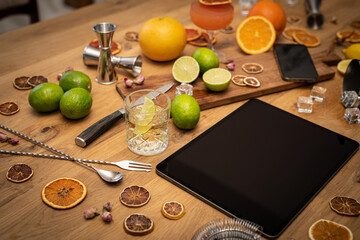 Online cocktail course with blank tablet, smartphone and bartender tools on wood kitchen table