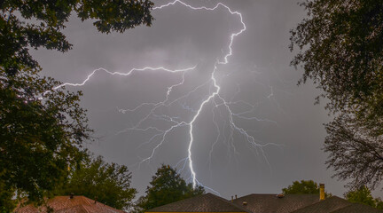 Canvas Print - Flash of lightning in the gray sky above the roofs of houses