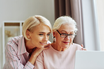 Close up portrait of young woman with senior mother using computer together at home and shopping online