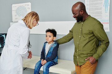 Wall Mural - Happy young African American man standing by his cute little son and looking at him in clinics while visiting radiologist or physician