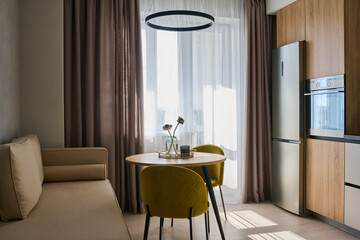 Wall Mural - Spacious kitchen in modern apartment with table and chairs standing in the center surrounded by beige sofa, refligerator and oven