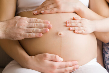 Wall Mural - Father and little daughter hands touching pregnant mother naked big belly and feeling future baby move. Cute moment. Emotional loving pregnancy time. Baby expectation. Closeup. Front view.