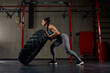Fit female athlete working out with a huge tire, turning and flipping in the gym. Woman exercising with big tire.