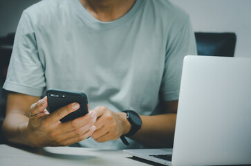 Wall Mural - man hand holding smartphone and computer laptop to working technology searching internet, sending sms, using text messenger or online banking.