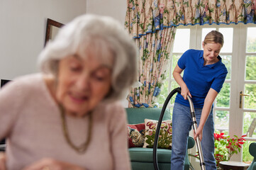 Wall Mural - Female Home Help Cleaning House With Vacuum Cleaner And Talking To Senior Woman