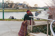 A gypsy woman in national dress rests by the river on the embankment in Krakow on a cloudy day