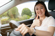 © DG PhotoStock - Happy Asian woman driving the electric vehicle - EV car smiling and showing her thumb up to the camera.