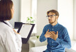 © Studio Romantic - Patient talking to doctor during consultation at hospital. Man sitting in exam room telling physician about chest pain. General practitioner listening to young male college student asking for advice