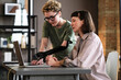 © AnnaStills - Young woman with prosthetic arm pointing at laptop and talking to her colleague during work at office