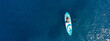 Aerial drone ultra wide panoramic photo with copy space of fit unidentified woman paddling on a SUP board or Stand Up Paddle board in deep blue sea