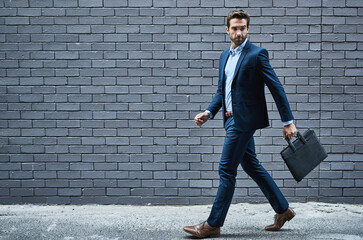 hes got the look. shot of a handsome young businessman standing against a grey facebrick wall.