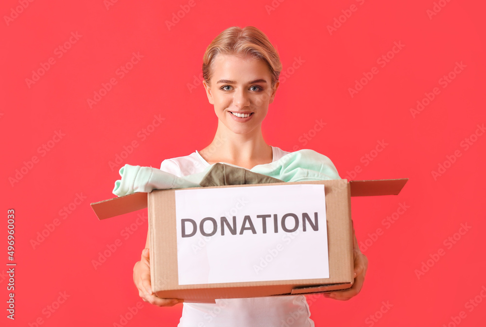 Young woman holding box with donation clothes on red background
