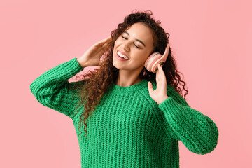 Wall Mural - Young African-American woman in headphones listening to music on pink background